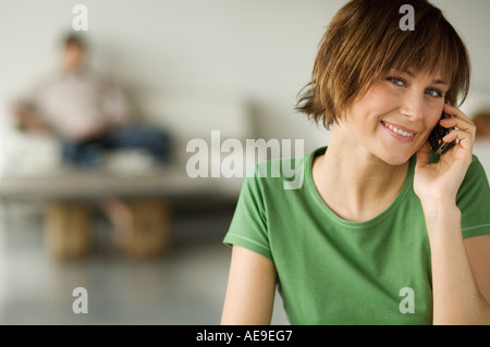 Smiling woman using mobile phone, man in the background Stock Photo