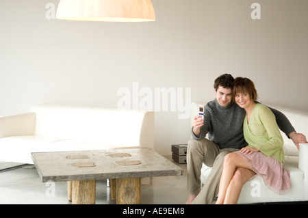 Smiling couple sitting on a sofa, taking picture with camera phone Stock Photo