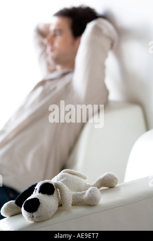 Thinking man sitting on a sofa, stuffed dog in the foreground Stock Photo