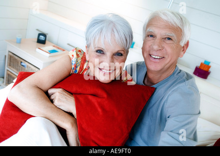 Senior couple sitting on a bed, smiling for the camera Stock Photo