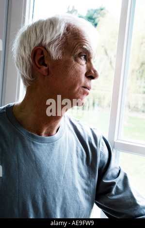 Thinking senior man looking through a window Stock Photo