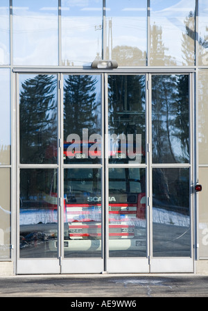 Fire department truck behind closed garage glass doors, forest reflecting from the glass , Finland Stock Photo