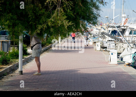 a standing man is partly obscured by hanging foliage in a yacht marina Stock Photo