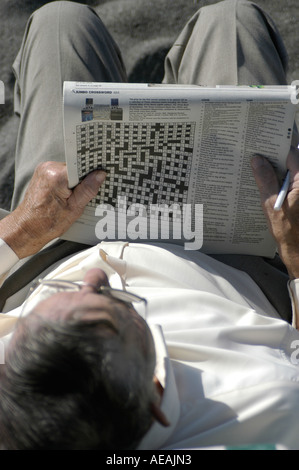 Man in his 50 s doing a jumbo bank holiday crossword in a broadsheet newspaper on the beach at Aberystwyth Stock Photo