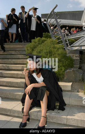 Woman graduate of Aberystwyth university drinks a glass of wine alone while sitting down after her graduation ceremony, Wales UK Stock Photo