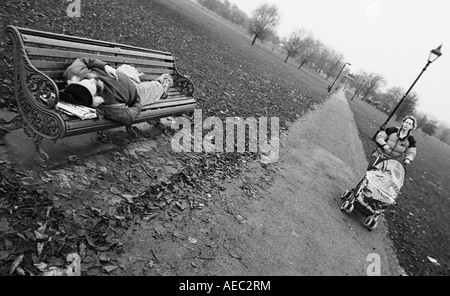 A tramp sleeps on a bench on Clapham Common as a London June 2005 Stock Photo