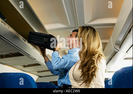 Couple stowing luggage in overhead compartment on airplane Stock Photo