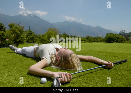 Woman laying on golf course with golf club and golf ball Stock Photo