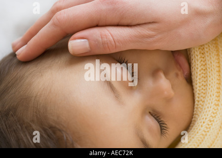 Close up of Hispanic sleeping baby with mother’s hand on cheek Stock Photo