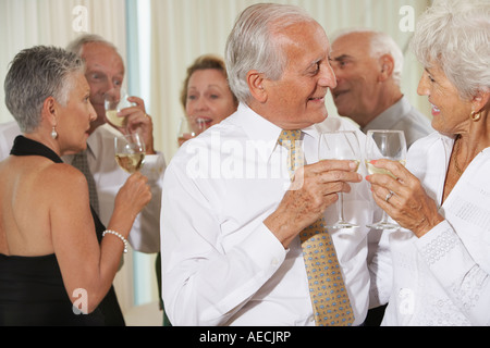 Senior couple toasting at party with friends in background Stock Photo