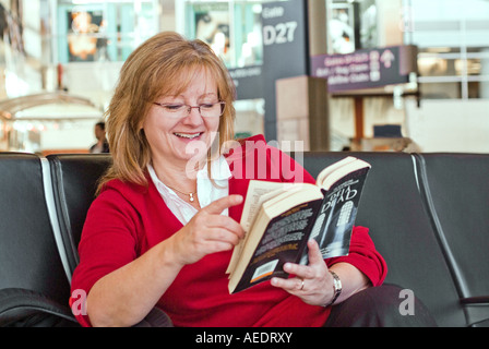 Attractive female sitting in airline terminal reading book Stock Photo