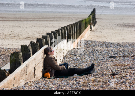 Person relaxing against the groynes on the beach Stock Photo