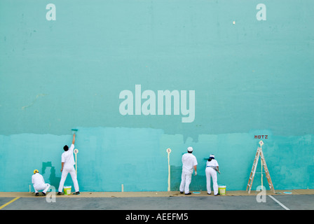Team of workers painting large blank wall turquoise for game of pelota, Spain Stock Photo