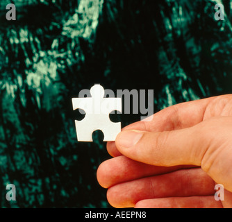 male hand holding a white jigsaw piece in his fingers which looks like a human body
