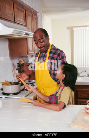 Dad and daughter working in 7-9 year old preparing pasta spaghetti dinner meal kitchen diverse diversity looking at each other smiling smile smiles POV  MR Stock Photo