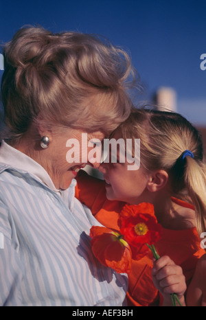 Grandparent child young girl, heads together smiling Caucasian older colorful red orange poppies flowers blue sky copy space closeup close up Stock Photo