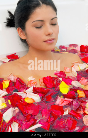 Hispanic woman with eyes closed in bath of flower petals Stock Photo