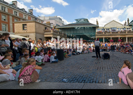 Horizontal wide angle of a street performer entertaining the crowds in the Piazza at Covent Garden on a bright sunny evening Stock Photo