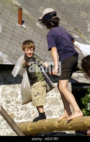 Two kids children boys wrestling with sand bags on wooden log outdoors. Stock Photo