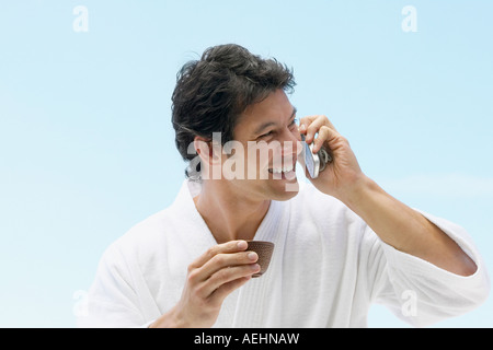 Asian man in spa bathrobe drinking tea and using cell phone Stock Photo