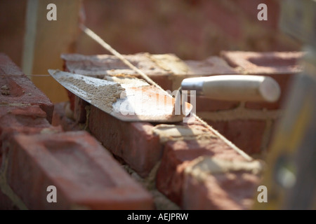 TROWEL LAYING ON BRICKS WITH MORTER ON A CONSTRUCTION SITE IN THE UK, BUILDING A HOUSE Stock Photo