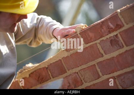 WORKER WITH HARD HAT LAYING BRICKS WITH MORTER ON A CONSTRUCTION SITE IN THE UK, BUILDING A HOUSE Stock Photo