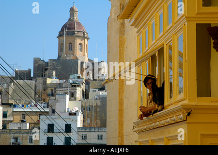 Local woman with a dog looking out a typical wooden balcony in the city of Senglea also known by its title Citta Invicta or Civitas Invicta in Malta Stock Photo