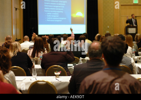 An unrecognizable crowd attends a business conference, listens to a speaker, and watches a presentation. Stock Photo