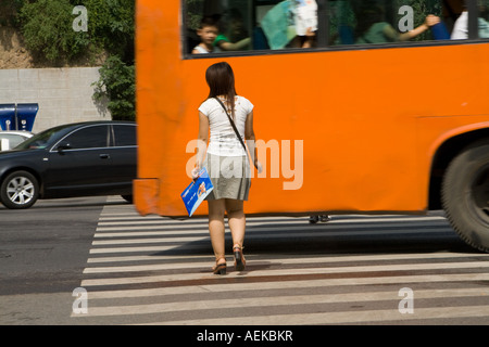 Woman pedestrian crossing busy road in front of a bus Xian, China Stock Photo