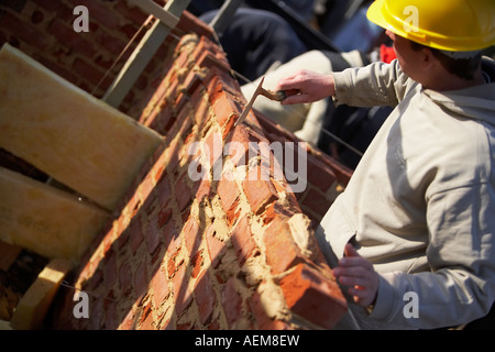 WORKER WITH HARD HAT LAYING BRICKS WITH MORTER ON A CONSTRUCTION SITE IN THE UK, BUILDING A HOUSE Stock Photo