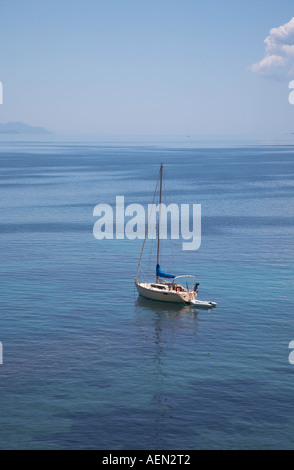 A lone yacht sails across the blue sea towards Corfu harbour Stock Photo