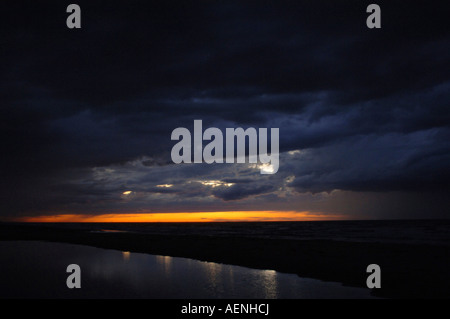 A beautiful shot capturing the sun setting behind a cloud on the beach. Stock Photo