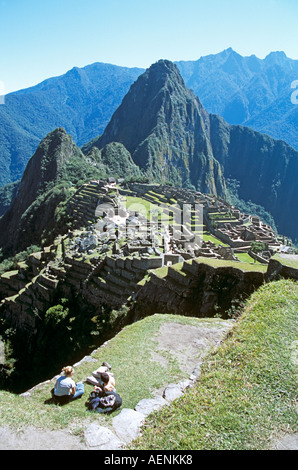 Machu Picchu Inca ruins, terraces, visitors relaxing and resting on ledge, and Huayna Picchu, Peru Stock Photo