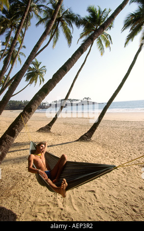 India Goa Palolem man in hammock beside palm fringed beach Stock Photo