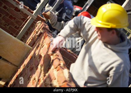 WORKER WITH HARD HAT LAYING BRICKS WITH MORTER ON A CONSTRUCTION SITE IN THE UK, BUILDING A HOUSE Stock Photo