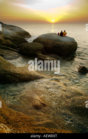 Two fishermen on rock at sunset, Kata Beach, Phuket Thailand Stock Photo