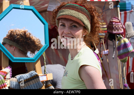 Girl at vending stall selling wollens, hat,  Young woman wearing & selling woolly hats on sunny day Portsoy, Morayshire near Inverness Scotland uk Stock Photo