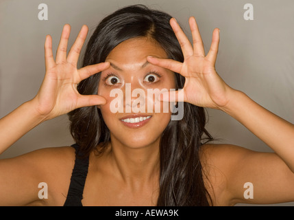 young  beautiful asian woman bulging the eyes with spread fingers Stock Photo