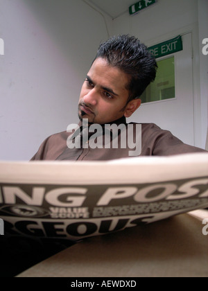 Young Asian man reading a sport section of daily newspaper at the workplace,London,England Stock Photo