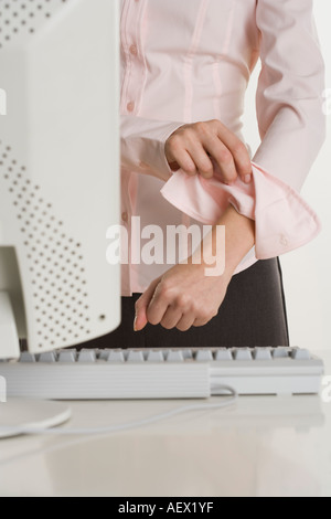 Woman rolling up sleeves at computer Stock Photo