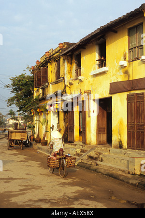 Woman in conical non hat cycling past old buildings in Bach Dang street at dawn, Hoi An, Viet Nam Stock Photo