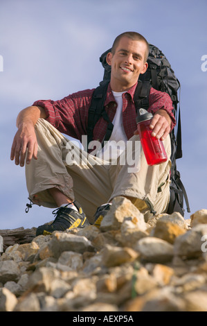 A hiker climber sits on top of a mountain and rests while holding a water jug and a backpack Stock Photo