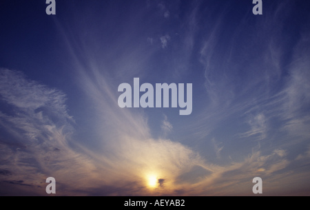 Yellow sun in cloud streaked sky Stock Photo