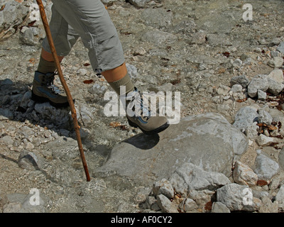 MR hiking in the mountains walking over stones scree with walking hiking shoes and stick trecking pole legs of a woman Stock Photo