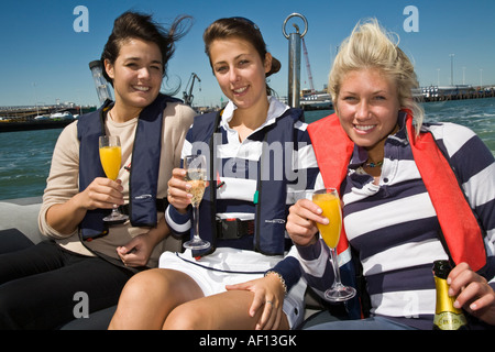 Three young ladies wearing lifejackets drinking and having fun on a power boat Stock Photo