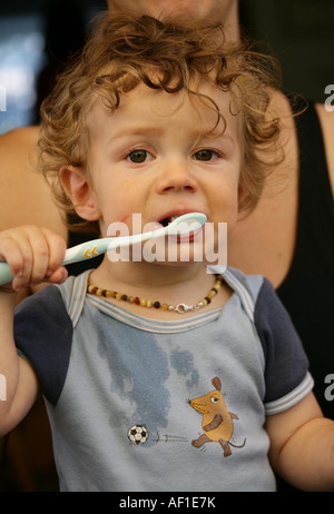 Kleinkind 18 Monate alt JONI mit Bernsteinkette putzt nach dem Essen mit verschmiertem Gesicht seine Milchzaehne Model Released Stock Photo