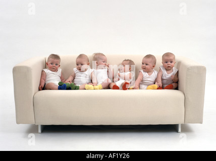 Six babies sitting on a sofa Stock Photo