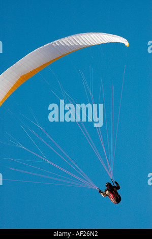 Pilot flying white and yellow paraglider against a perfectly blue sky support lines are perfectly lit against the blue sky Stock Photo