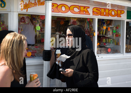 A Muslim woman eats ice cream and checks her mobile phone on the pier at Brighton Sussex England Stock Photo