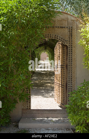 Ornate wooden door and foliage laden wall leading to garden in luxury villa, Marrakesh, Morocco